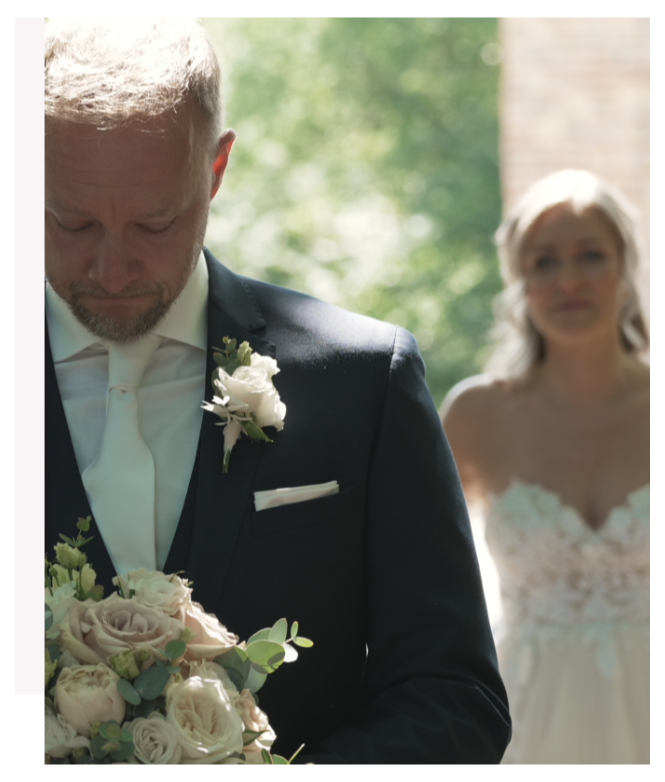 Bruidegom met een boeket in zijn handen, met de bruid op de achtergrond in een lichte omgeving.